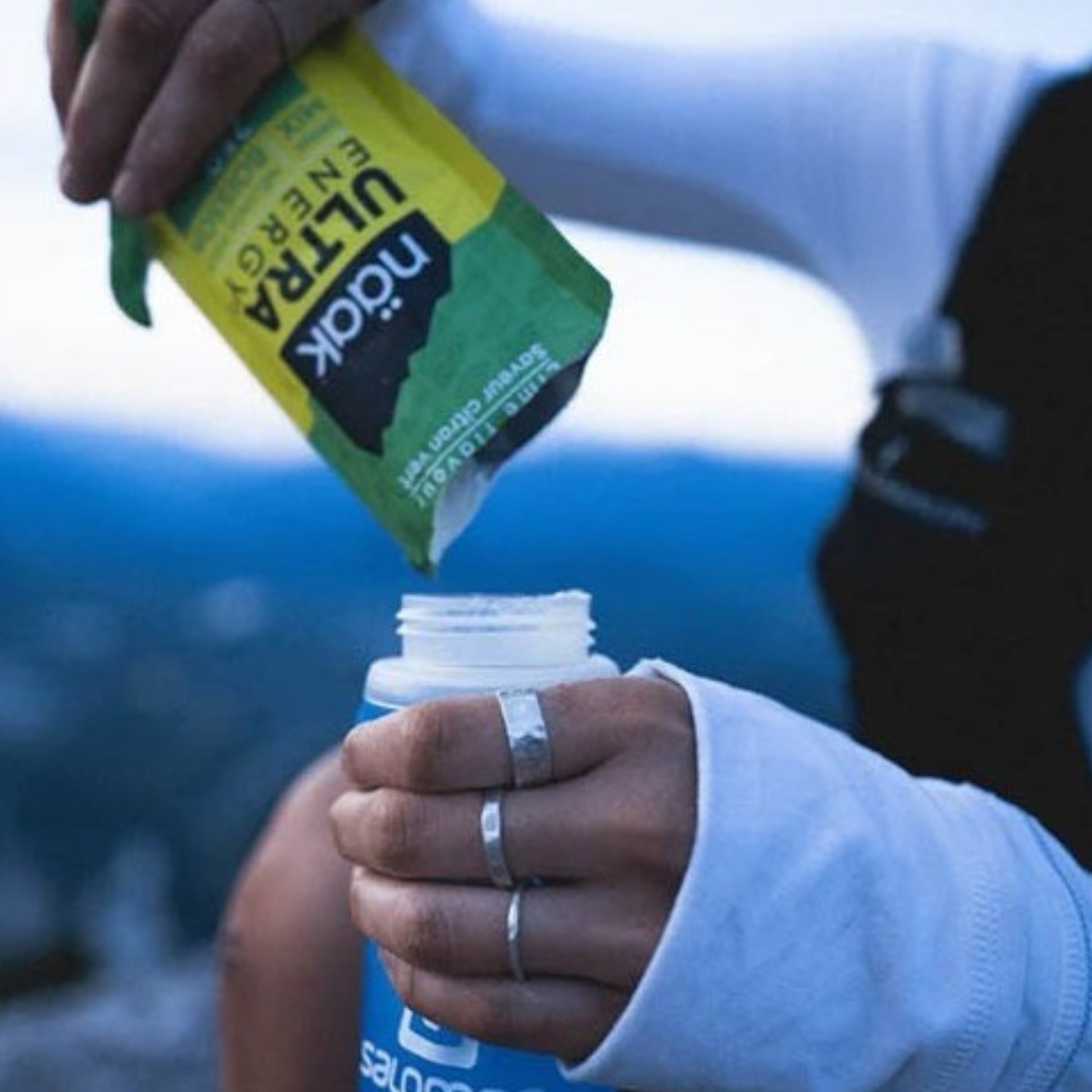 Person pouring Ultra Naak from a green packet into a bottle with a blurred background